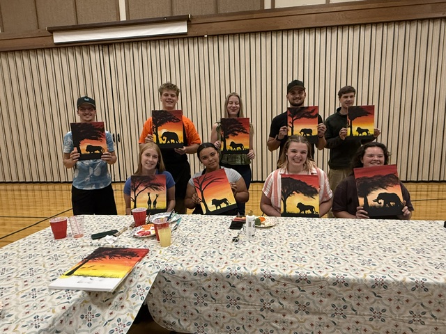Young single adults holding up their finished sunset canvases at the end of the evening